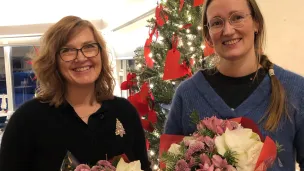 To kvinner med blomsterbuketter foran juletre