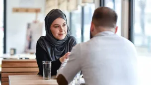 Kvinne med hijab og mann med ryggen til sitter på kafe