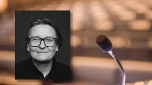 Portrettfoto av Ragnhild Hennum, dekan ved UiO, mot bakgrunn med mikrofon og tomme stolrader