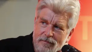 Portrettfoto av forfatter Karl Ove Knausgård med mikrofon mot oransje bakgrunn