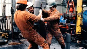 Tre arbeidere i verneutstyr jobber med boring på oljeplattform