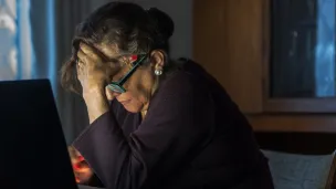 Eldre kvinne med bøyd hode foran pc'n
