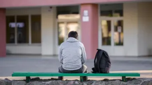Gutt sittende med ryggen til på en benk i skolegården