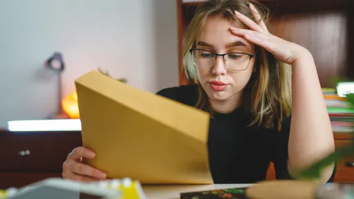 Jente eller ung kvinne med blondt og hår og briller som ser stresset ut og holder papir i den ene hånda