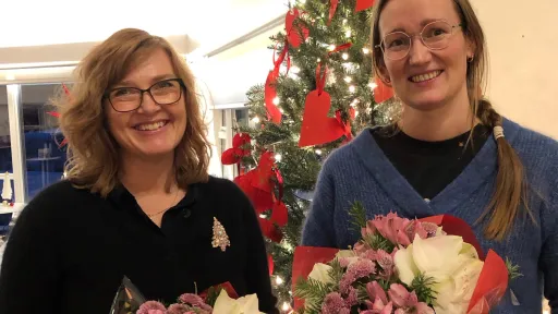 To kvinner med blomsterbuketter foran juletre