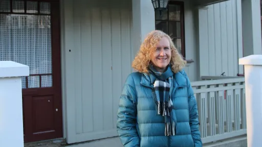 Kvinne i blå boblejakke foran et gammelt hus