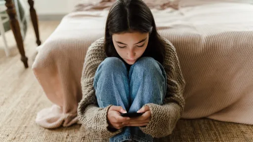 Ung jente sitter på gulvet og leser på mobilen sin