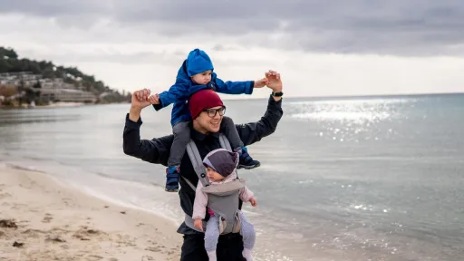 Pappa på tur på stranden med ett barn i bæresele og ett på nakken