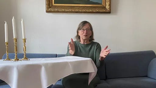 Charlotte Koren sittende i blå sofa ved et bord med hvit duk