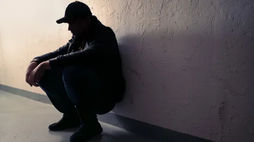 Mann sitter på huk inntil en vegg
