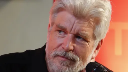 Portrettfoto av forfatter Karl Ove Knausgård med mikrofon mot oransje bakgrunn