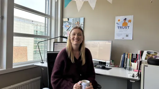 Andrea Norvoll Rustand stipendiat ved Nasjonalt kunnskapssenter om vold og traumatisk stress, sitter på kontoret sitt med en kaffekopp i fanget