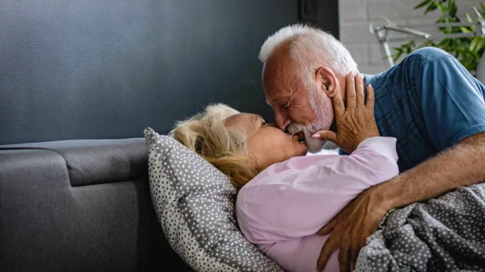 Eldre mann med skjegg omfavner eldre kvinne i en seng