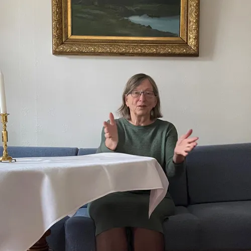 Charlotte Koren sittende i blå sofa ved et bord med hvit duk