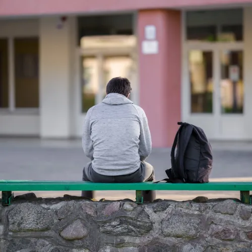 Gutt sittende med ryggen til på en benk i skolegården