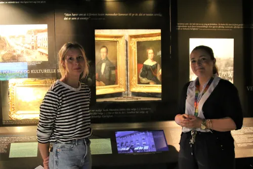 Helene Huljev og Therese Johnsen i foran tablået med bildene av Camilla Collett og ektemannen Jonas Collett i Oslo bymuseum.